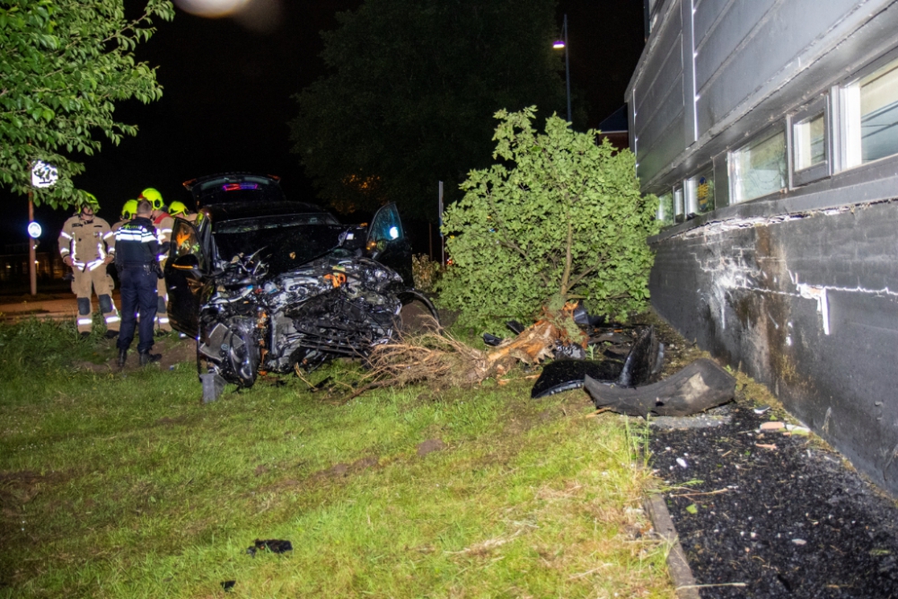 Auto rijdt boom uit de grond en knalt tegen muur